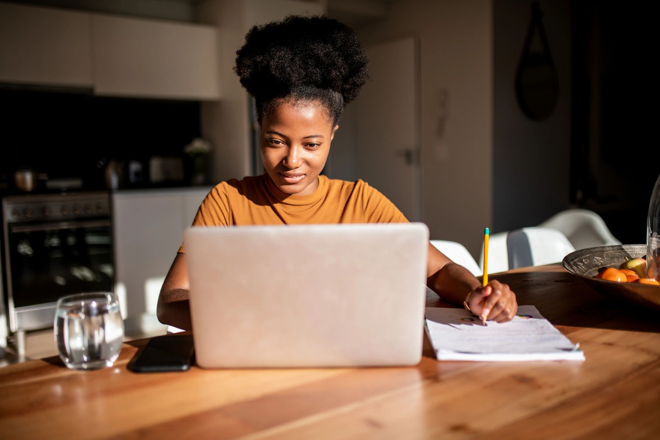 Student taking notes while learning online on a laptop